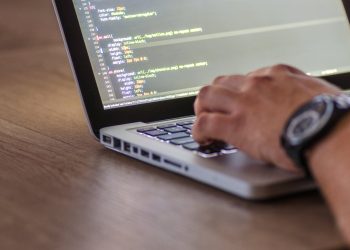 A close-up shot of a person coding on a laptop, focusing on the hands and screen.